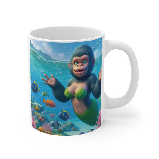White ceramic mug featuring a cute smiling monkey mermaid swimming underwater among colorful tropical fish and coral reefs.