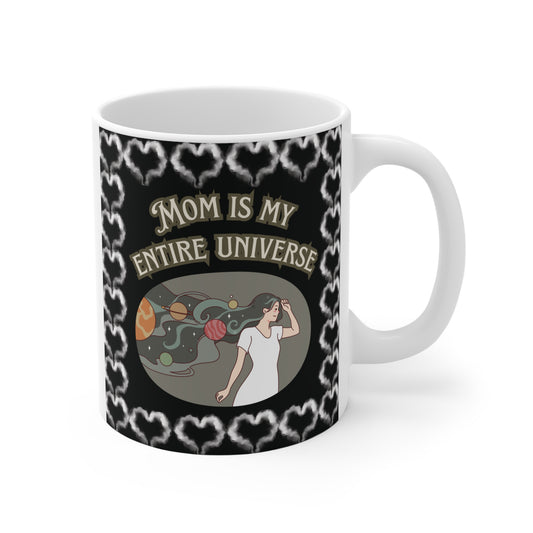 Ceramic coffee mug featuring a celestial "Mom is my entire universe" design with a woman whose hair flows into a galaxy of planets and stars, bordered by white smoky hearts.
